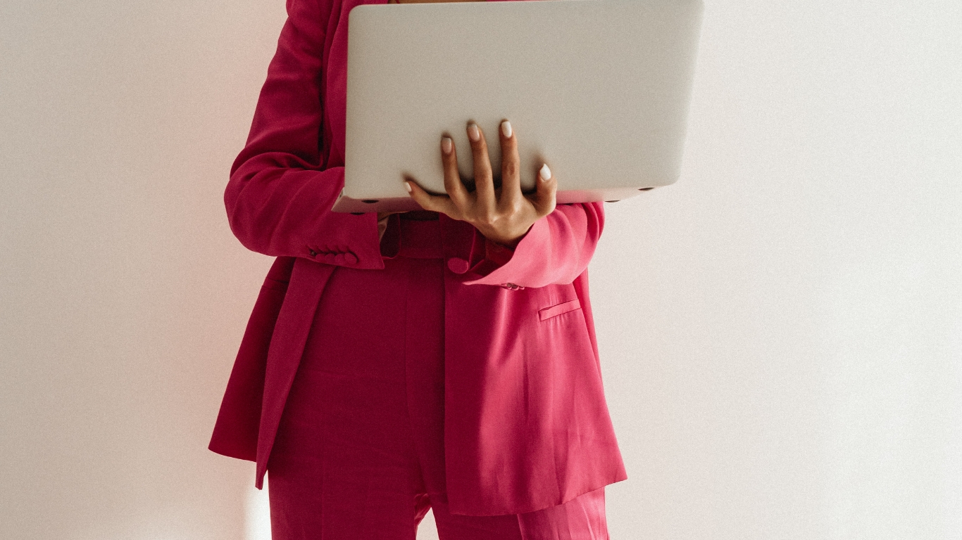 photo d'une business woman en tailleur rose fuchsia tendance portant dans les mains un MacBook